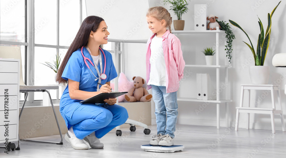 Obraz premium Female pediatrician with little girl measuring weight in clinic