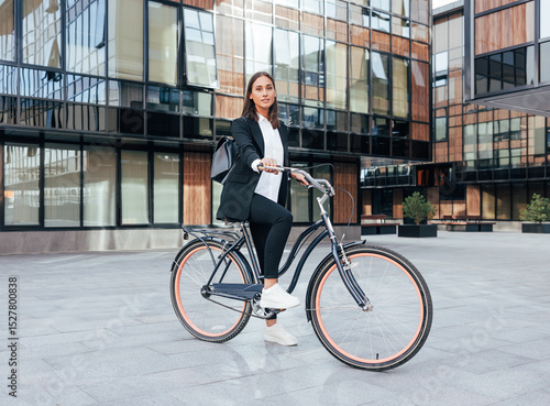 Stylish businesswoman with a bicycle standing in the city wearing a backpack and black office attire