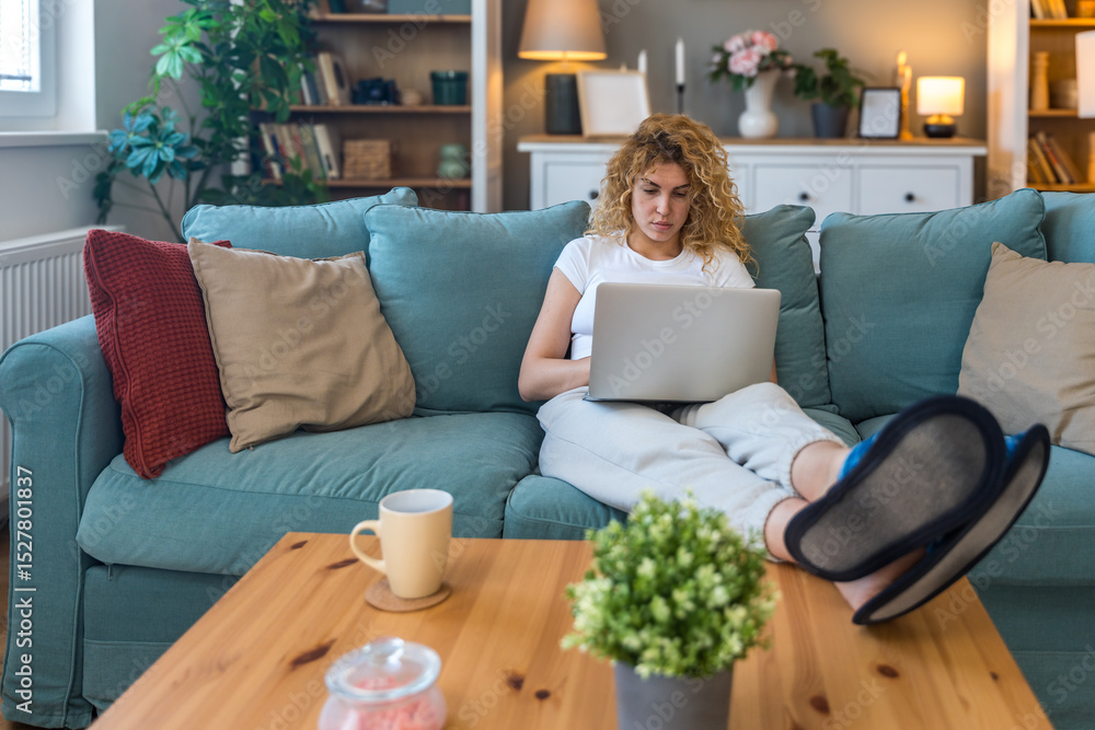 Young university student working side hustle to pay rent and costs of living as translator. Woman translating text on her laptop computer while sitting on sofa at home. Female typing online message. Young university student working side hustle to pay rent and costs of living as translator. Woman translating text on her laptop computer while sitting on sofa at home. Female typing online message.