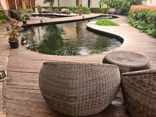 A koi fish pond in a public area with nearby empty rattan chairs, offering a peaceful and quiet moment in a commercial environment.
