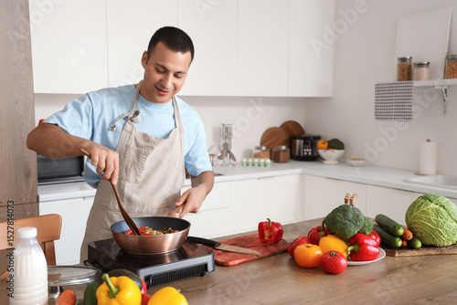 Young man frying vegetables...