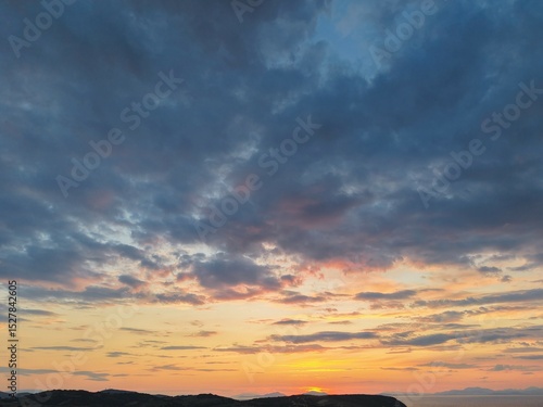 Beautiful cloudy red sunrise over sea with beach, waves and mountains in the background. Impressive structure texture in the sky