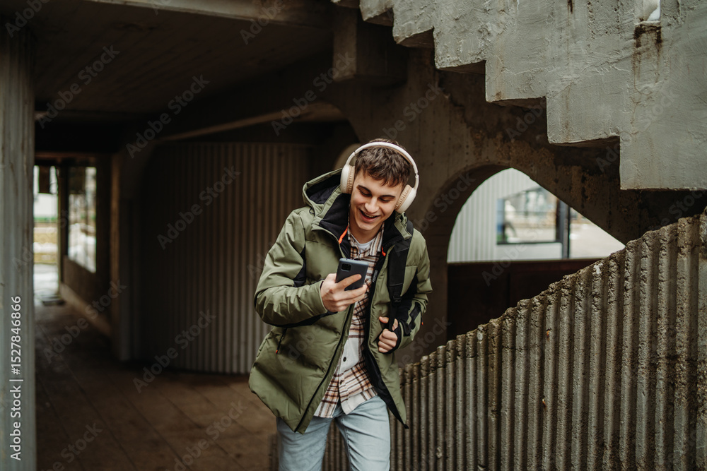 Fototapeta premium Young adult caucasian man student smile with phone and headphones on university stairs 