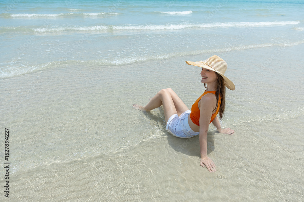 custom made wallpaper toronto digitalYoung smiling women with straw hat, orange top and white shorts sitting on beach in tropical location with blue sky and turquoise sea.