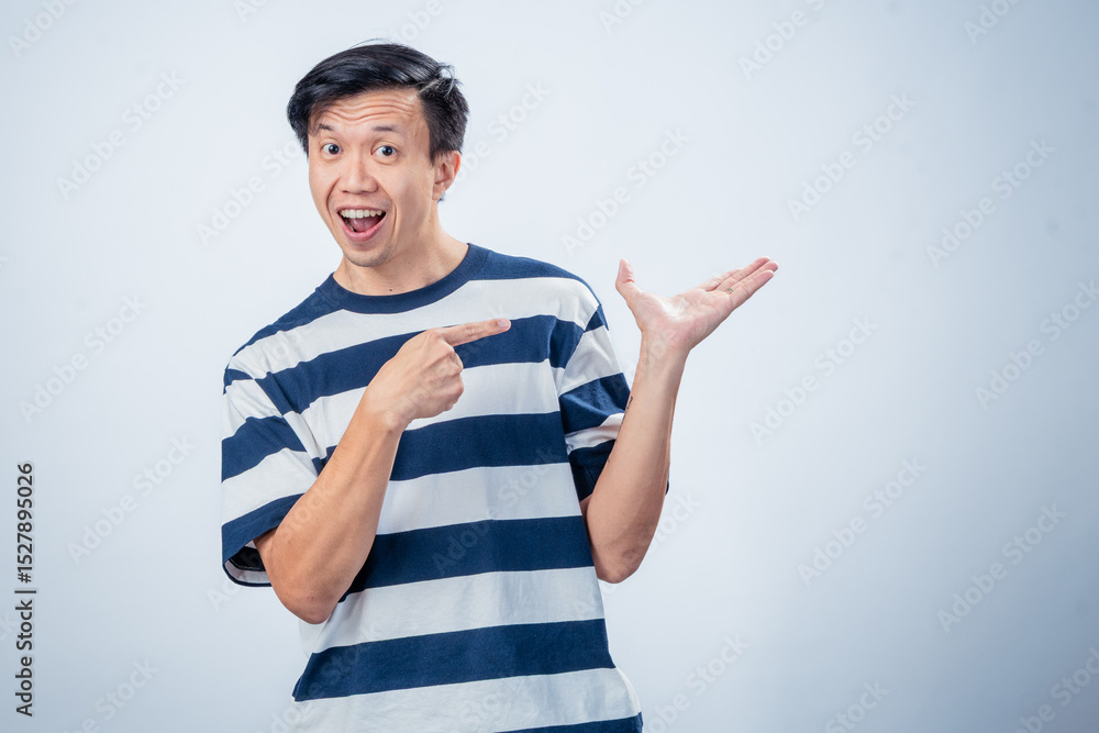Asian man in striped shirt smiling and pointing excitedly to his open palm, posing against a plain light background in a promotional or presenting gesture Asian man in striped shirt smiling and pointing excitedly to his open palm, posing against a plain light background in a promotional or presenting gesture