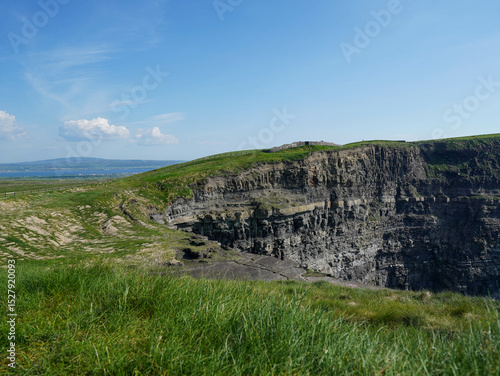 A steep cliff edge meets the rolling grassy hills under a peaceful blue sky