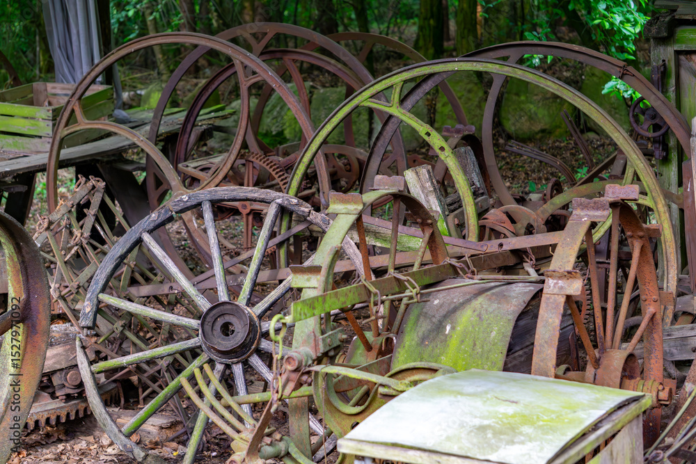 collection of old, rusty metal wheels and agricultural machinery parts lying in the forest. The components are covered with moss and rust, creating a scene of forgotten technology in a natural settin collection of old, rusty metal wheels and agricultural machinery parts lying in the forest. The components are covered with moss and rust, creating a scene of forgotten technology in a natural settin
