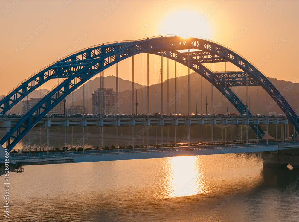 Naklejka premium Evening panorama of a blue arch bridge with moving cars over calm water at sunset. Hangzhou, China.