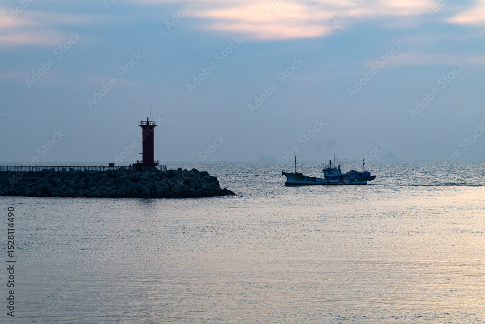 Fototapeta premium fishing boat and lighthouse at the harbor during sunset
