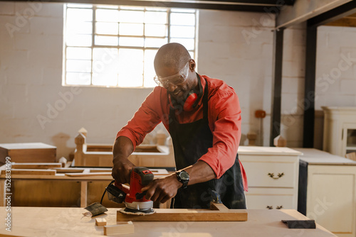 Electric hand sander gliding across wooden plank on sturdy workbench in workshop with natural light