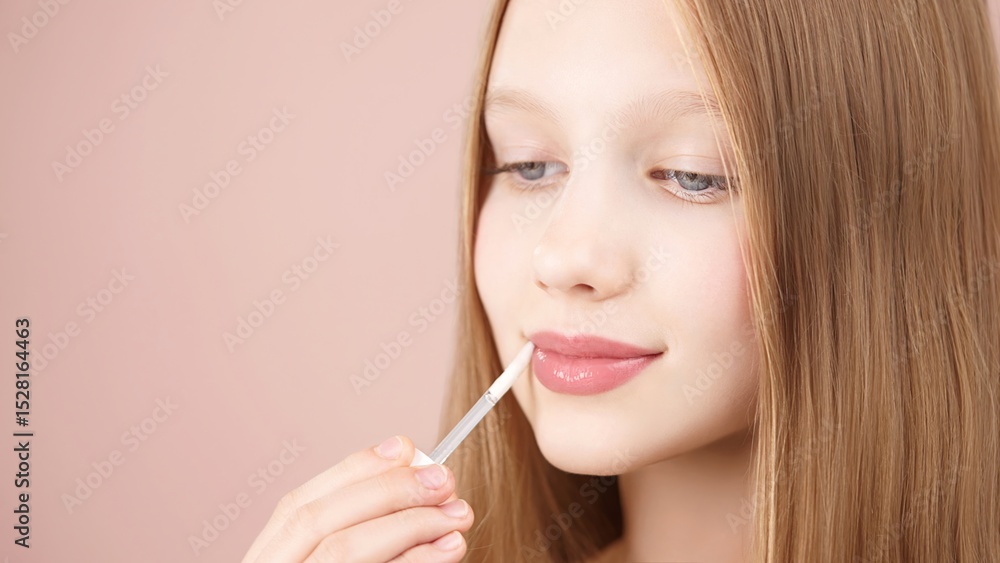 Cute young girl applying lip gloss. Caucasian blonde girl gen Alpha with blue eyes using make-up cosmetics, posing in studio on pink background. Concept of advertising cosmetics for teens. Copy space. Cute young girl applying lip gloss. Caucasian blonde girl gen Alpha with blue eyes using make-up cosmetics, posing in studio on pink background. Concept of advertising cosmetics for teens. Copy space.