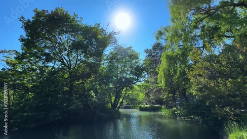 Serene view of the river flowing through Sapporo Nakajima Park, bright sun and lush trees