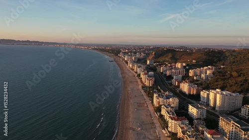 Forward-moving drone shot over Durres Beach in Albania, showing turquoise waters, sandy shoreline, resort umbrellas, and the bustling cityscape stretching along the Adriatic coast.