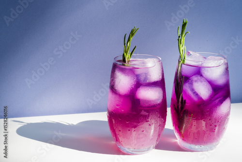 Glasses with freshly made purple cocktails with ice and rosemary stand on table.