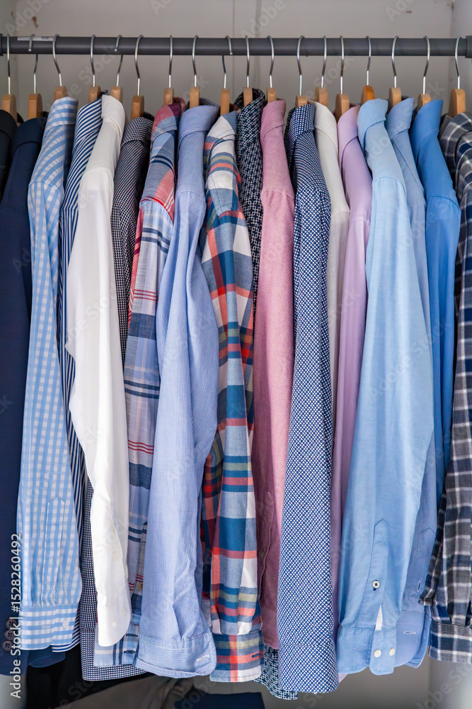 Neatly arranged men shirts hanging on wooden hangers in wardrobe. Minimalist clothing organization and classic male fashion concept Neatly arranged men shirts hanging on wooden hangers in wardrobe. Minimalist clothing organization and classic male fashion concept