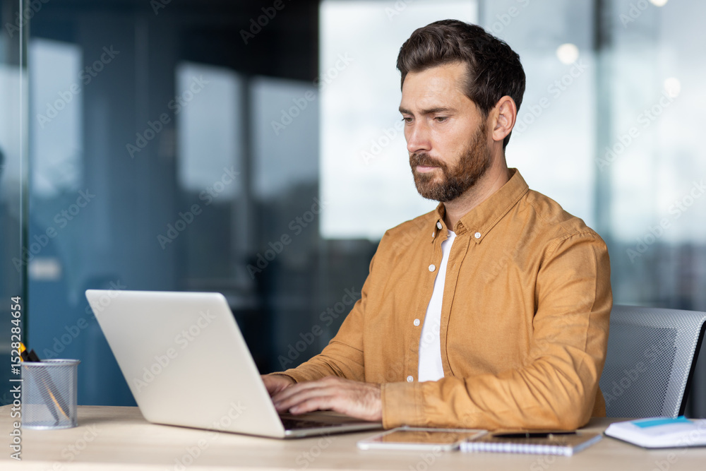 Fototapeta premium A focused businessman working on a laptop in an office environment, showcasing concentration and productivity.