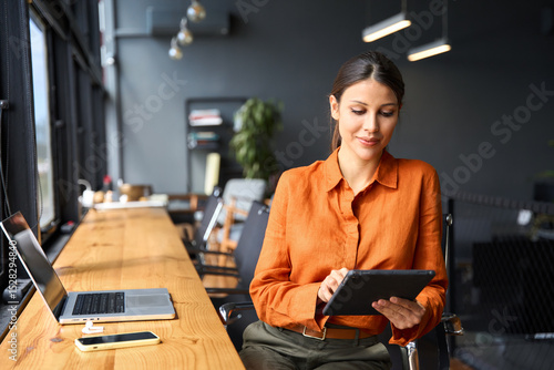 Fotografie Successful smiling latin hispanic young woman using pad computer for business app