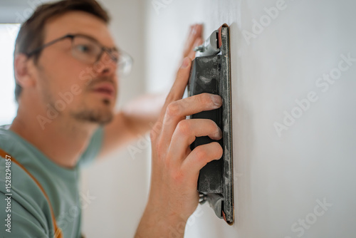 Photography Construction worker smoothing a white wall with an electric sander, preparing th