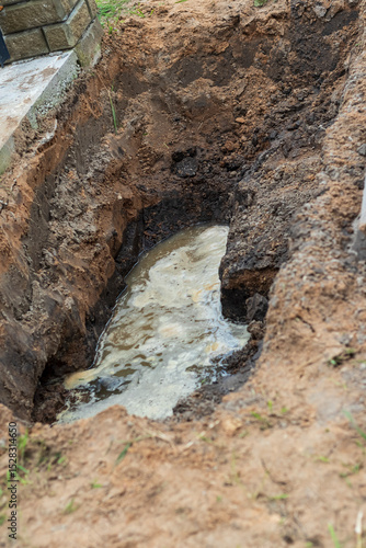 Leak from a broken water pipe in a trench near a construction site causing disruption and potential damage