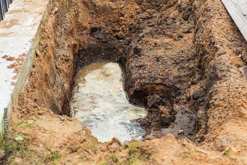 Leak from a broken water pipe in a trench near a construction site causing disruption and potential damage