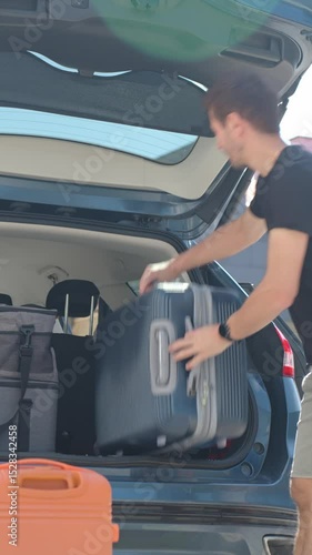 Man loading suitcases into car trunk near suburban house. Preparing for travel by packing luggage into vehicle. Concept of relocation or road trip