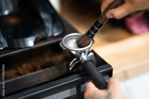 Barista cleaning portafilter with brush, close-up, isolated in cafe workspace.