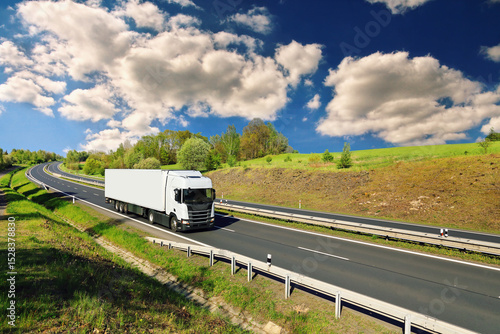 A truck with semi-truck drives through a wide landscape