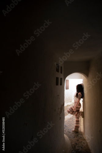 Young girl in pants leans against a door frame in the sunset sunlight of the fishing village of Binibeca