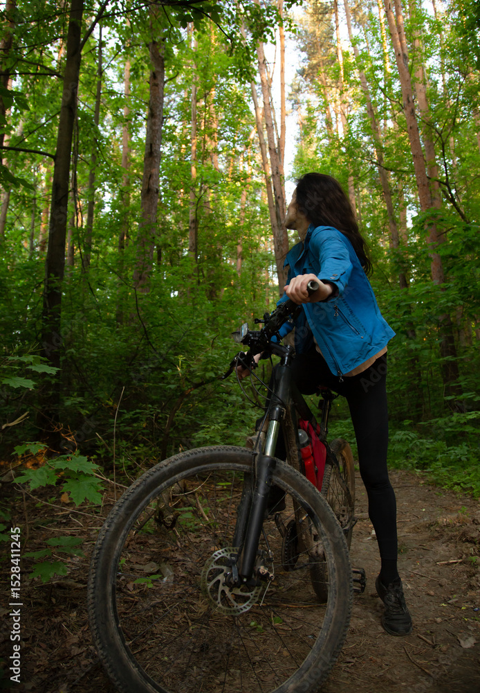Fototapeta premium Beauty smiling woman biking on bicycle on spring trees green forest background, looking back. Enjoying fun girl outdoors. Female cyclist riding in park in sport fashion clothes. Full lenght