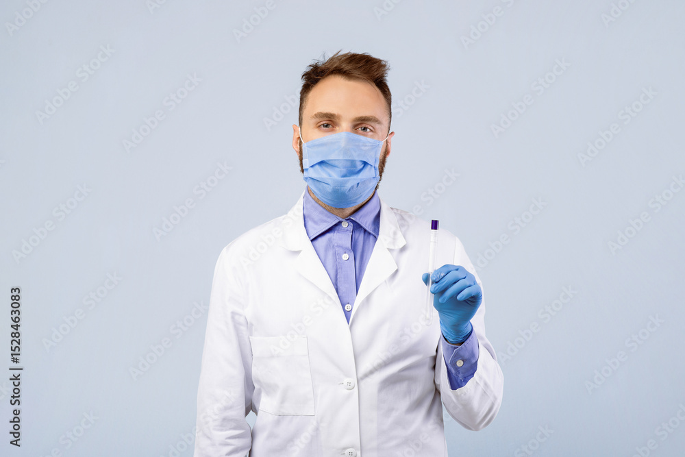 Millennail male doctor in protective mask and gloves holding sterile swab stick for coronavirus PCR test on grey studio background. Young medic with tube for nasal and oral covid diagnostic procedure Millennail male doctor in protective mask and gloves holding sterile swab stick for coronavirus PCR test on grey studio background. Young medic with tube for nasal and oral covid diagnostic procedure