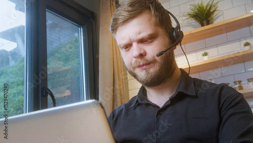 Bearded man wearing a headset looks at his laptop with a confused or concerned expression, likely during a virtual meeting or tech support.