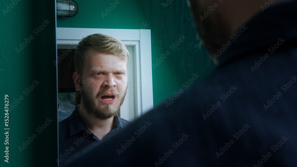 Fototapeta premium Troubled man appears to argue with his reflection in bathroom mirror, suggesting internal conflict, mental struggle, or emotional crisis.