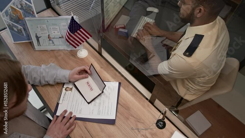 View from above of male submission officer returning rejected visa application to frustrated young man and proceeding to work on computer