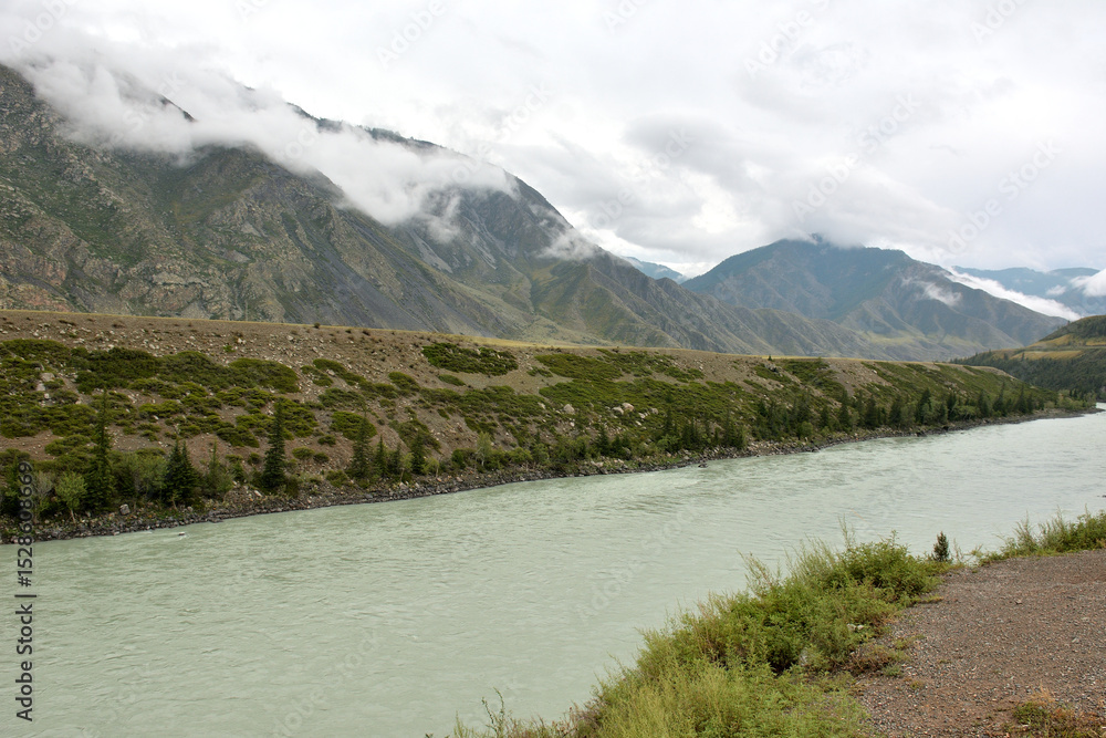 Obraz premium Thunderclouds low over a picturesque mountain valley with a beautiful river flowing through it on a sunny summer day.