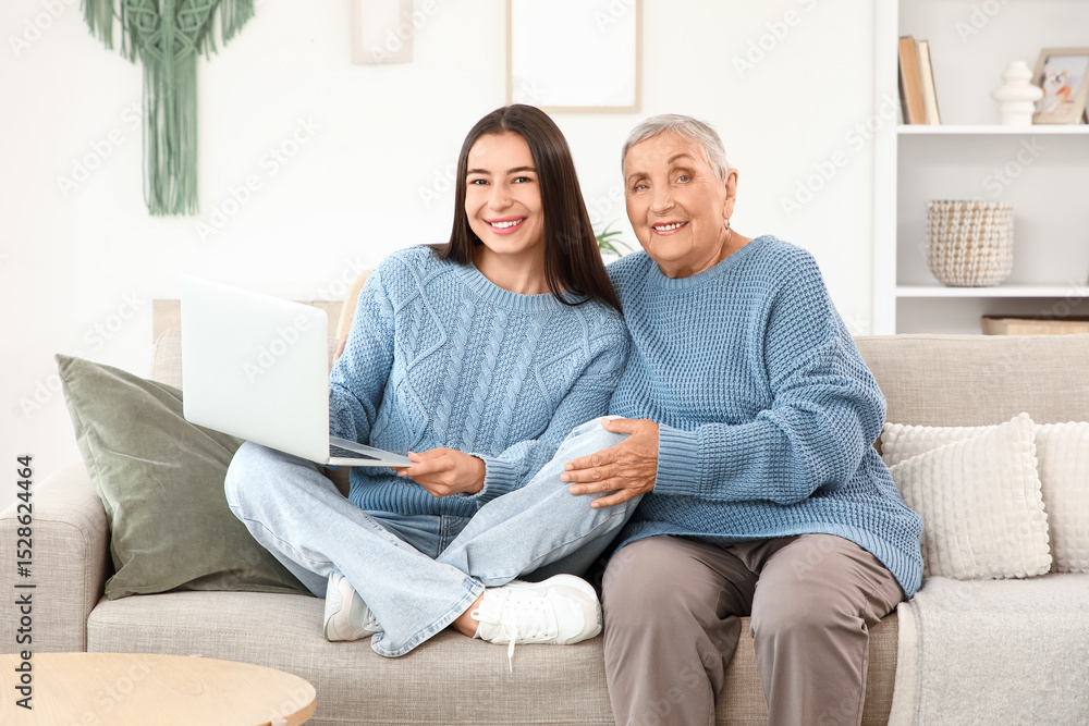 Happy young woman with laptop and her grandmother sitting on sofa at home Happy young woman with laptop and her grandmother sitting on sofa at home