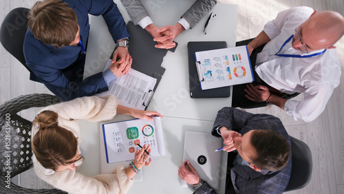 The board of Directors is sitting at a table with papers and laptops, top view. They discuss ideas and work together on a project