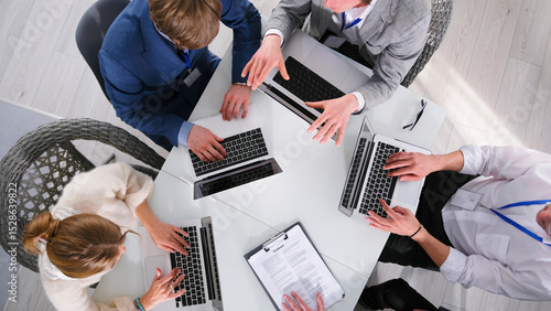 A consulting firm is working on a major project, top view. A group of people are sitting at a table with their laptops open