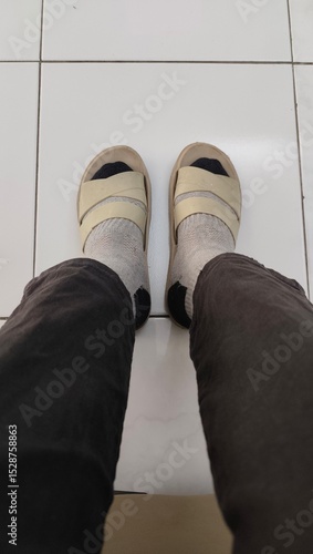 A pair of legs wearing black pants,  socks and brown sandals