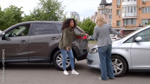 Irritated African American woman driver and nervous middle aged woman emotionally arguing after car accident on city street , blaming each other for vehicle collision