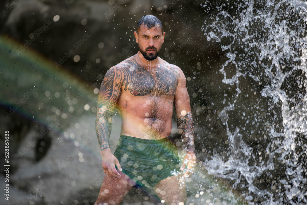 Fototapeta premium Powerful man on nature. Sexy shirtless man splashing under waterfall. Fit and strong male body in nature. Sexy model enjoying summer. Male beauty. Muscular torso with water drops. Topless guy in