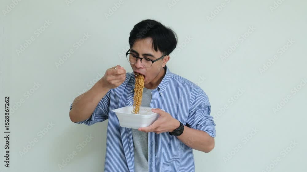 Happy young Asian man eating noodles and smiling with joy. Studio shot capturing authentic expression of enjoyment, ideal for food, lifestyle, or advertisement themes Happy young Asian man eating noodles and smiling with joy. Studio shot capturing authentic expression of enjoyment, ideal for food, lifestyle, or advertisement themes