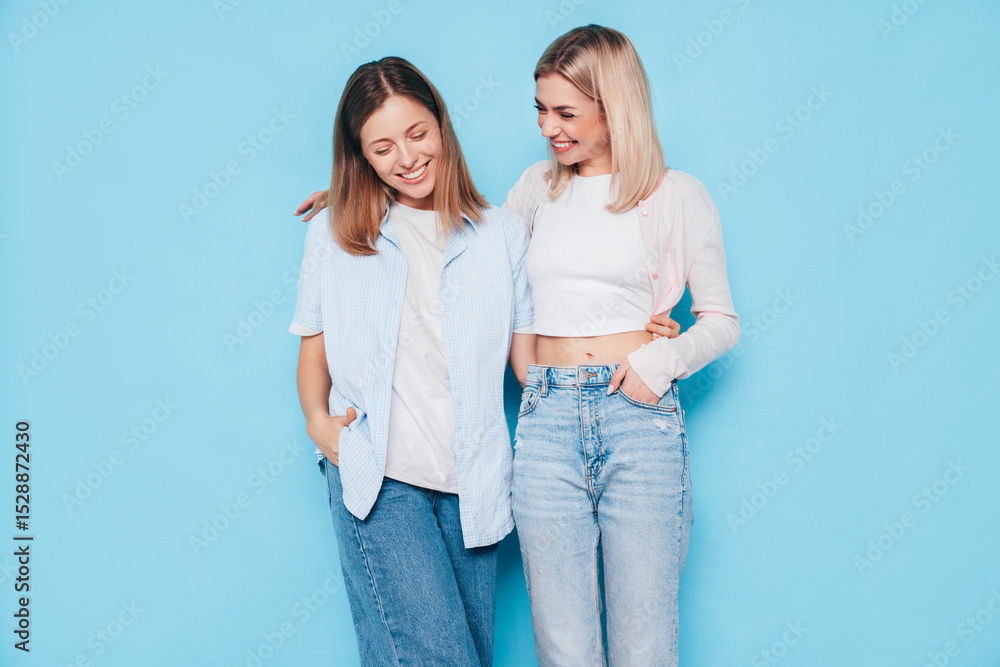 Two young beautiful smiling brunette hipster female in trendy summer clothes. Lovely women posing on blue background in studio. Positive models having fun. Cheerful and happy. isolated Two young beautiful smiling brunette hipster female in trendy summer clothes. Lovely women posing on blue background in studio. Positive models having fun. Cheerful and happy. isolated