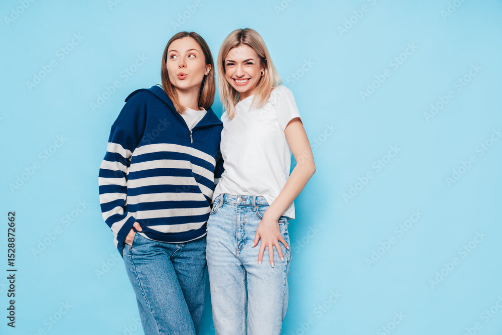 Two young beautiful smiling brunette hipster female in trendy summer clothes. Lovely women posing on blue background in studio. Positive models having fun. Cheerful and happy. isolated Two young beautiful smiling brunette hipster female in trendy summer clothes. Lovely women posing on blue background in studio. Positive models having fun. Cheerful and happy. isolated