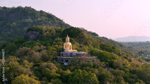 Wallpaper Mural Aerial shot showing a massive golden seated meditating Buddha on Hat Sai Noi mountain at sunset, surrounded by green tropical forest in Hua Hin, Thailand  Torontodigital.ca