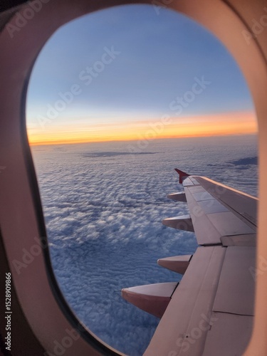 Aerial view from inside a flying airplane, capturing the wing stretching out above the clouds under the open sky.