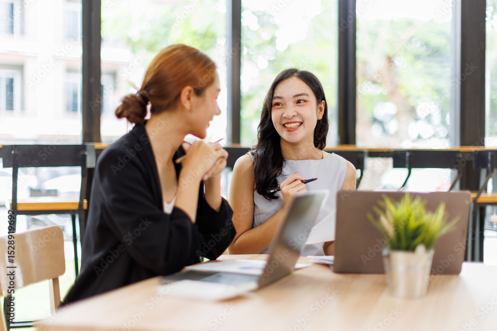 Obraz premium Two asian business women in teamwork discussing and using laptop in the office . Two excited happy asian business women are talking and consulting.