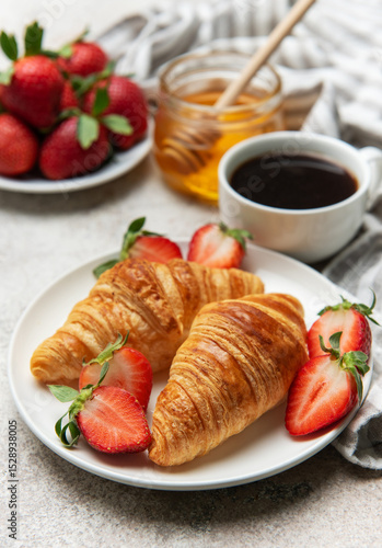 Delicious french breakfast with coffee, honey and croissants accompanied by fresh strawberries