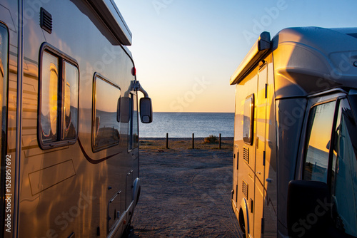 Two motorhomes bathed in early morning sunlight at a beach in Spain. Camper and motorhome holiday image. Camping car. Hymer.