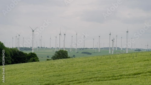Windkraftanlagen in grüner Hügellandschaft bei bewölktem Himmel