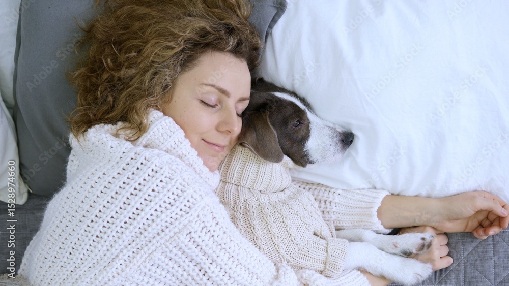 Woman with curly hair peacefully sleeps next to her dog, both wearing cozy knitted sweaters, enjoying a restful moment together in a comfortable bed covered with white sheets Woman with curly hair peacefully sleeps next to her dog, both wearing cozy knitted sweaters, enjoying a restful moment together in a comfortable bed covered with white sheets